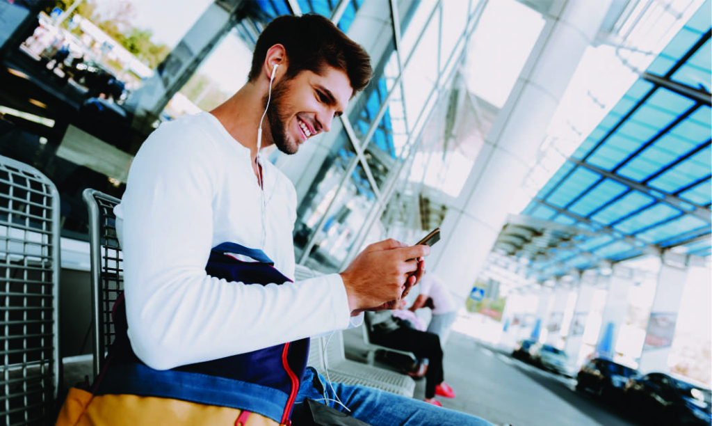 Young man sitting on a bench in the pickup area at an airport looking at his phone